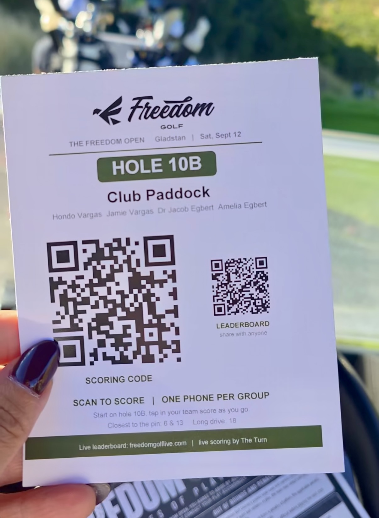 A golfer at The Freedom Open, Gladstan Golf Course, holding up the cart sign with the QR code that opens her team scorer.